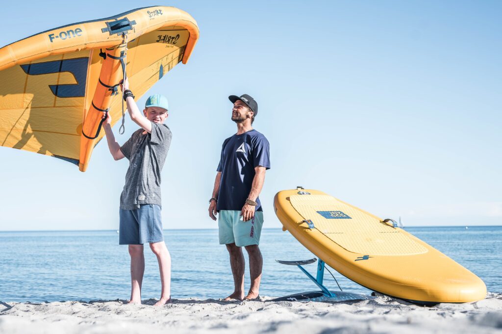 Wingfoil Coach und Schüler am Strand mit Wingfoil in der Hand. Wingfoil Kurse an der Ostsee